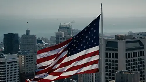 Large American flag flying above a city skyline.